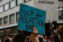 someone holding a poster on a demonstration with the words "fuck your abortion ban" written on it
